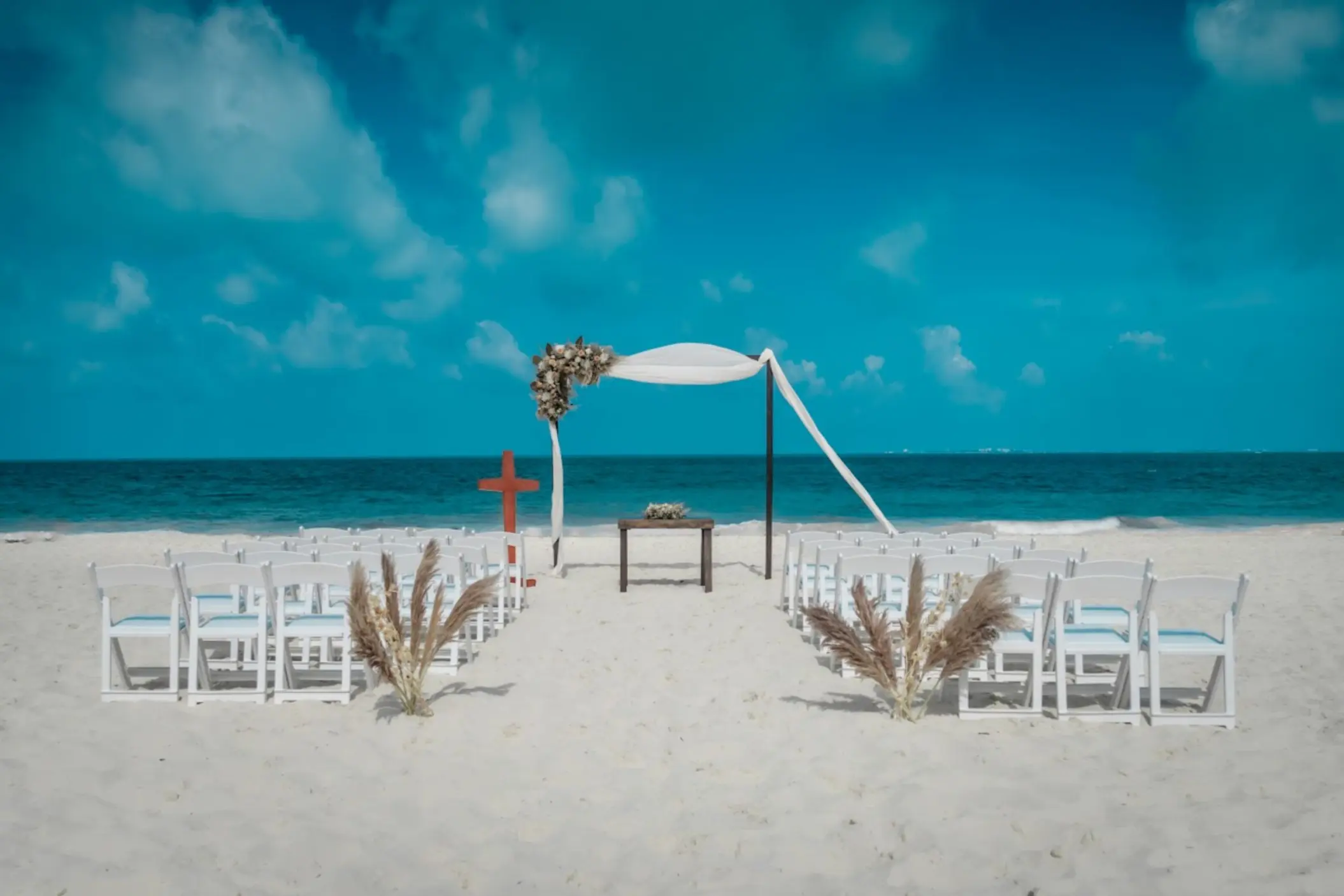 Beachfront wedding ceremony with white chairs and floral arch at Catalonia Grand Costa Mujeres, Cancun
