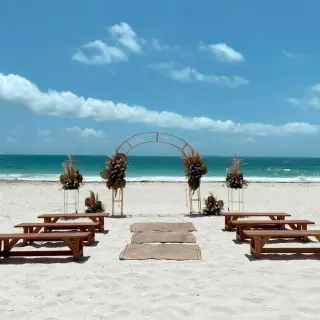 Beachfront wedding ceremony with a circular arch and wooden benches at Catalonia Grand Costa Mujeres, Cancun