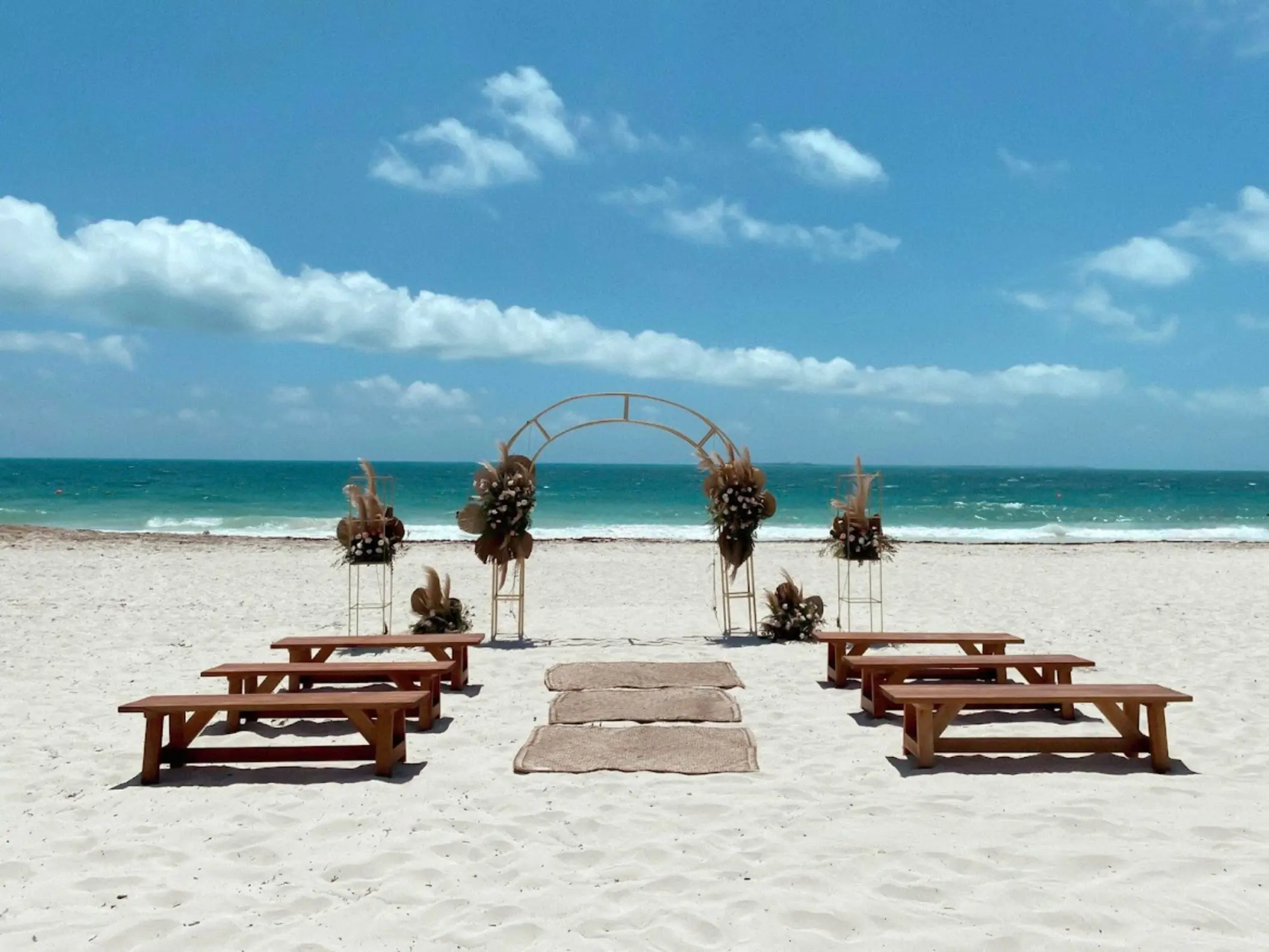 Beachfront wedding ceremony with a circular arch and wooden benches at Catalonia Grand Costa Mujeres, Cancun