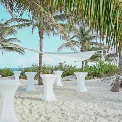 Beachfront wedding reception setup with cocktail tables under palm trees at Catalonia Grand Costa Mujeres, Cancun