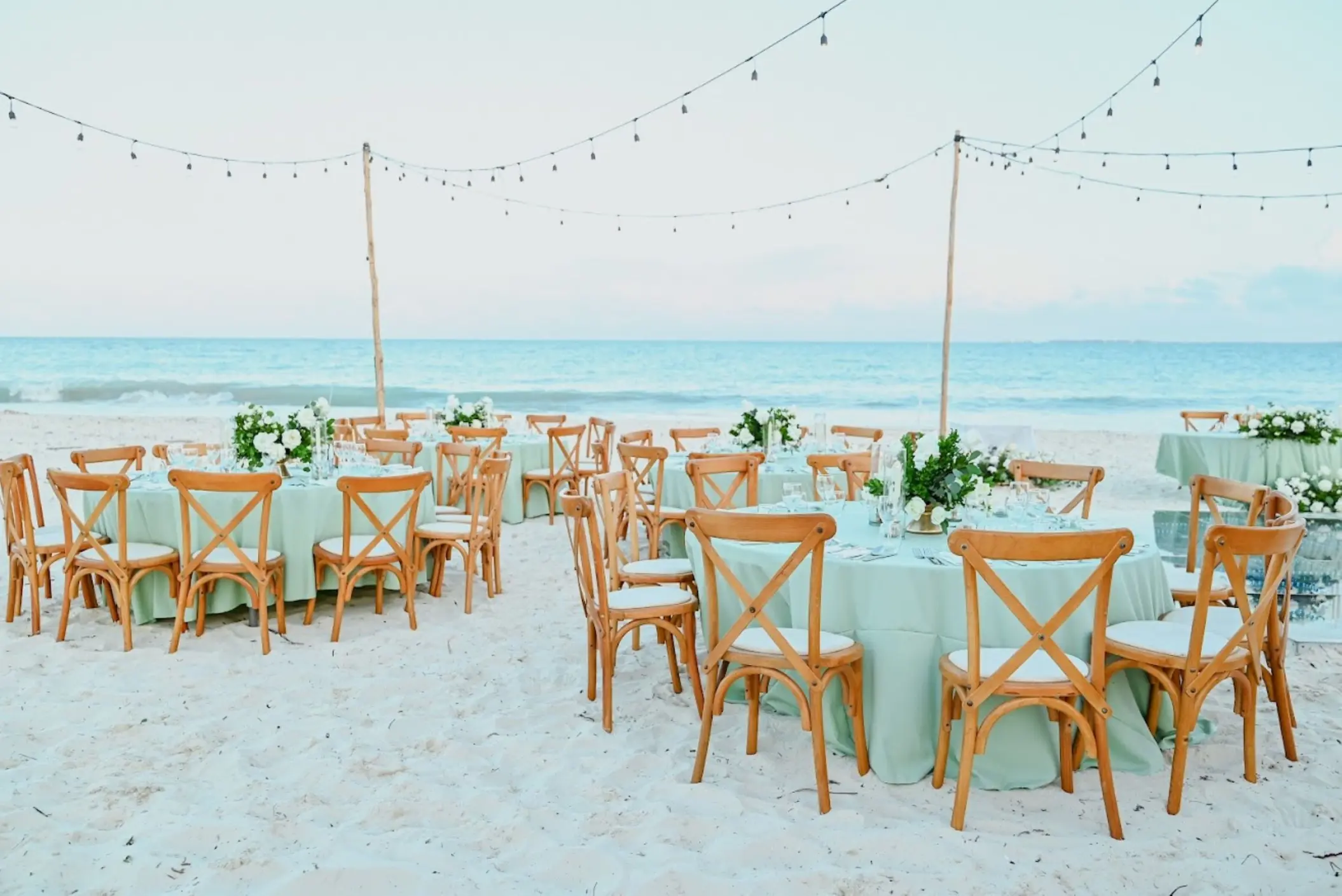 Beachfront wedding reception with round tables and string lights at Catalonia Grand Costa Mujeres, Cancun