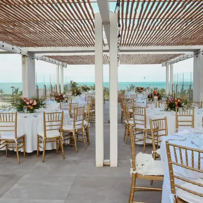 Terrace wedding reception with gold chairs under a wooden pergola at Catalonia Grand Costa Mujeres, Cancun