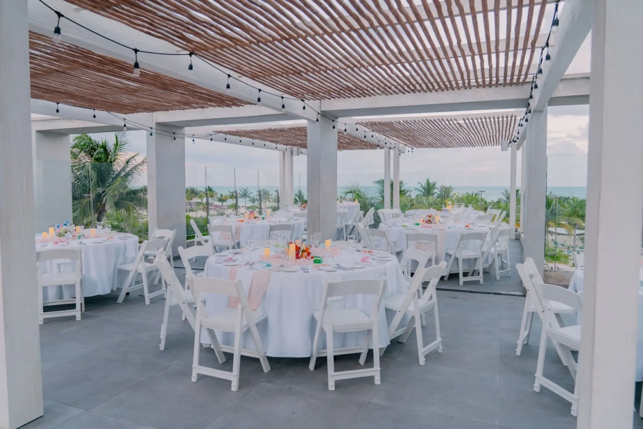 Rooftop wedding reception with round tables and white chairs under a pergola at Catalonia Grand Costa Mujeres, Cancun