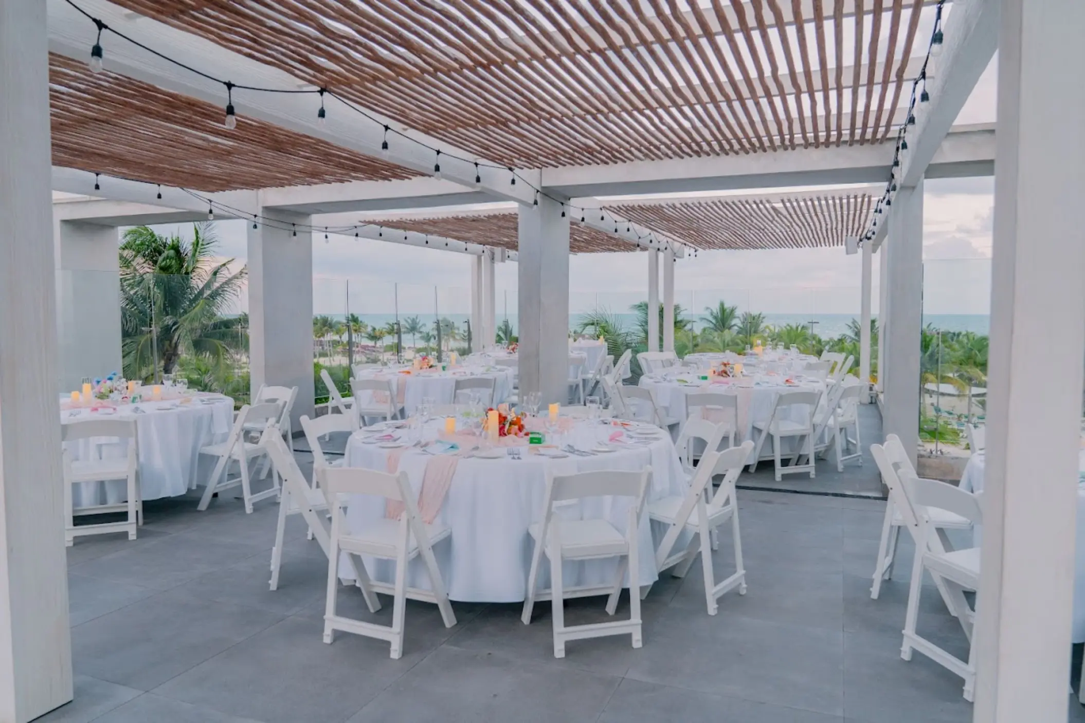 Rooftop wedding reception with round tables and white chairs under a pergola at Catalonia Grand Costa Mujeres, Cancun