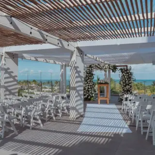 Terrace wedding ceremony under a pergola with white chairs and floral arch at Catalonia Grand Costa Mujeres, Cancun