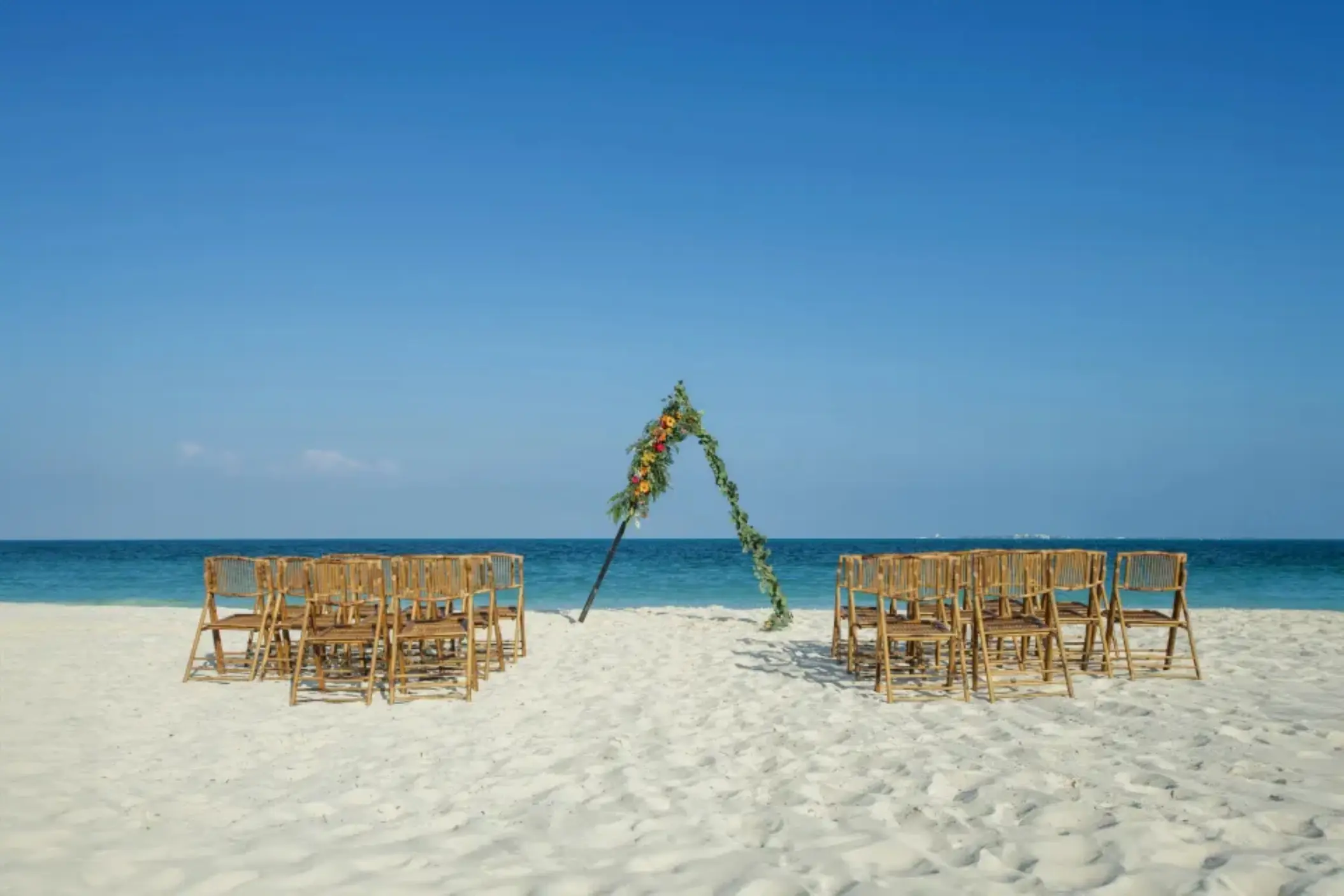 Beachfront wedding ceremony setup with triangular floral arch and bamboo chairs at Catalonia Montego Bay