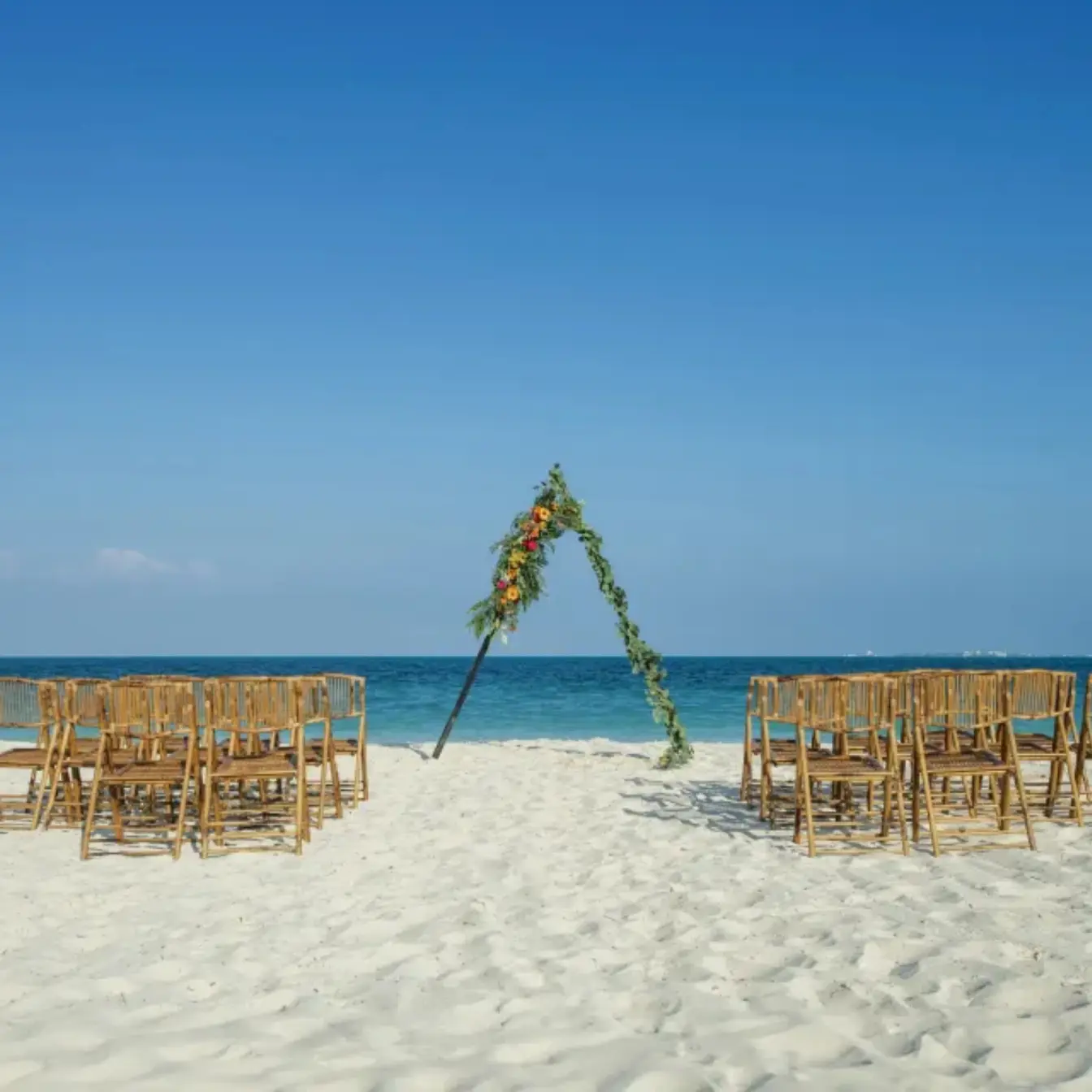 Beachfront wedding ceremony setup with triangular floral arch and bamboo chairs at Catalonia Montego Bay