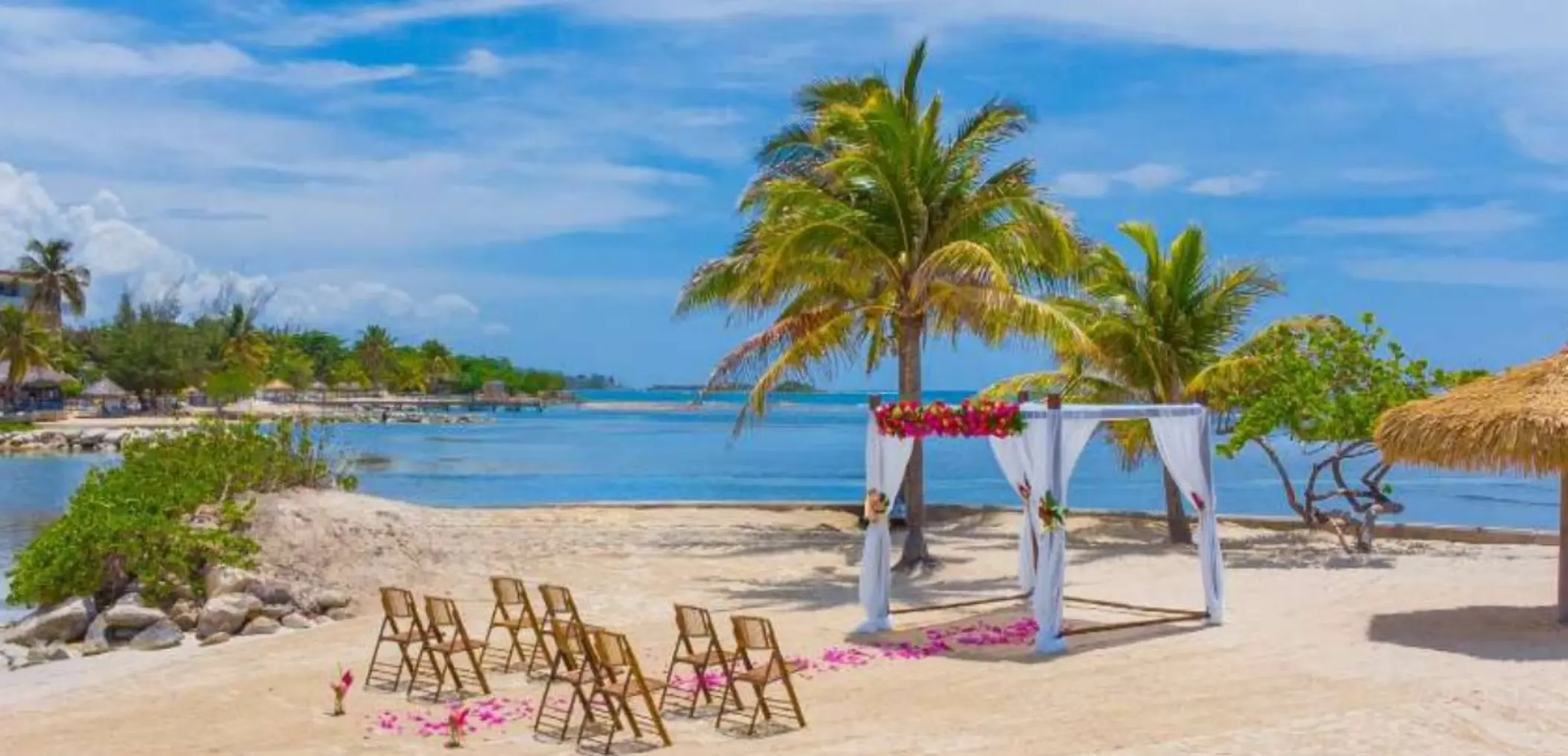 Beachfront wedding ceremony with a floral huppah and wooden chairs at Catalonia Montego Bay, Montego Bay