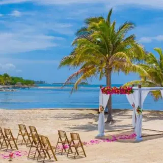 Beachfront wedding ceremony with a floral huppah and wooden chairs at Catalonia Montego Bay, Montego Bay
