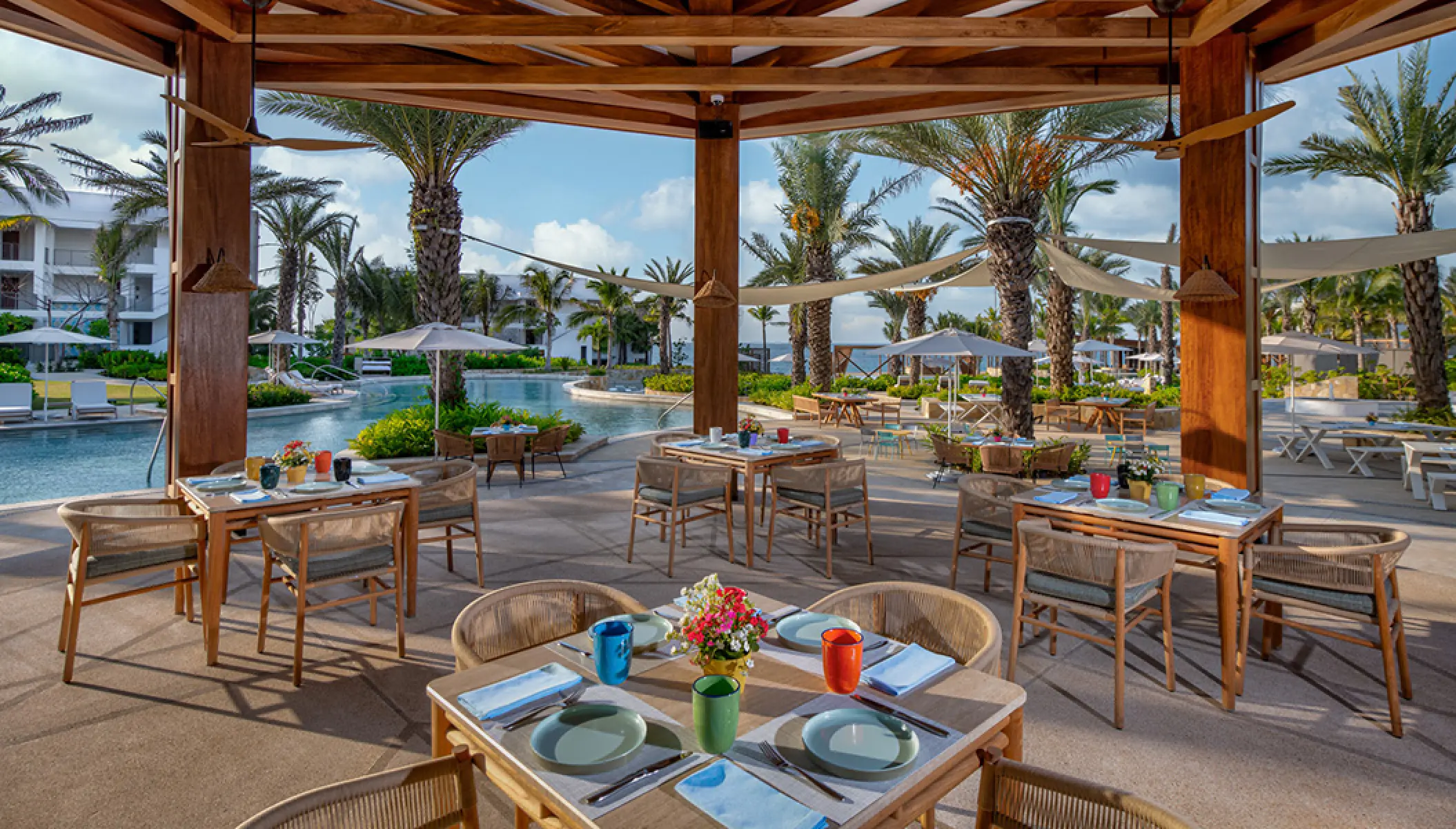 Open-air restaurant with wooden tables and chairs overlooking the pool at Conrad Punta de Mita, Puerto Vallarta