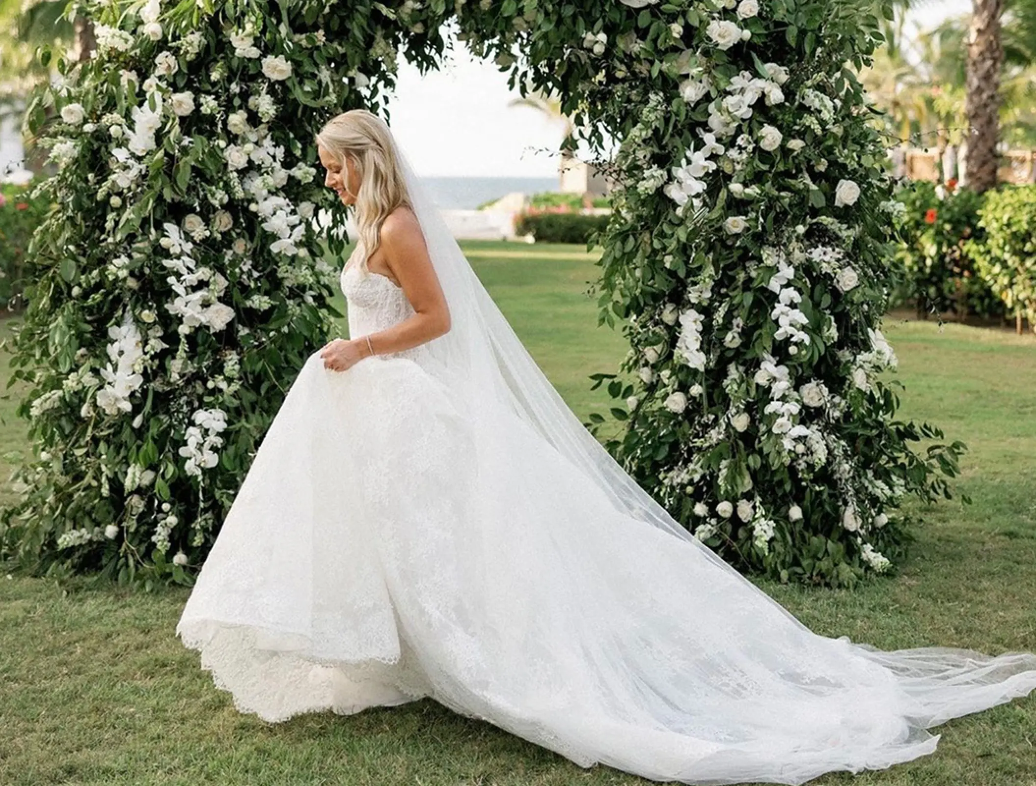 Bride walking past a floral wedding arch at Conrad Punta de Mita, Puerto Vallarta