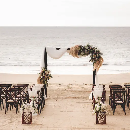 Beach wedding ceremony with a floral arch and wooden cross-back chairs at Conrad Punta de Mita, Puerto Vallarta