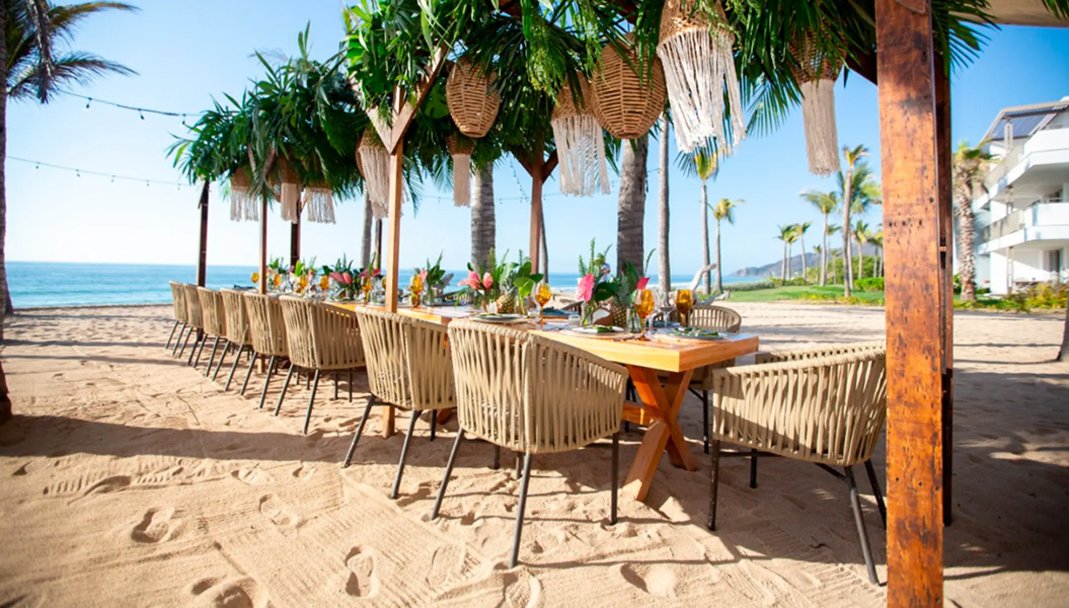 Beachfront wedding reception setup with wooden tables and woven chairs at Conrad Punta de Mita, Puerto Vallarta