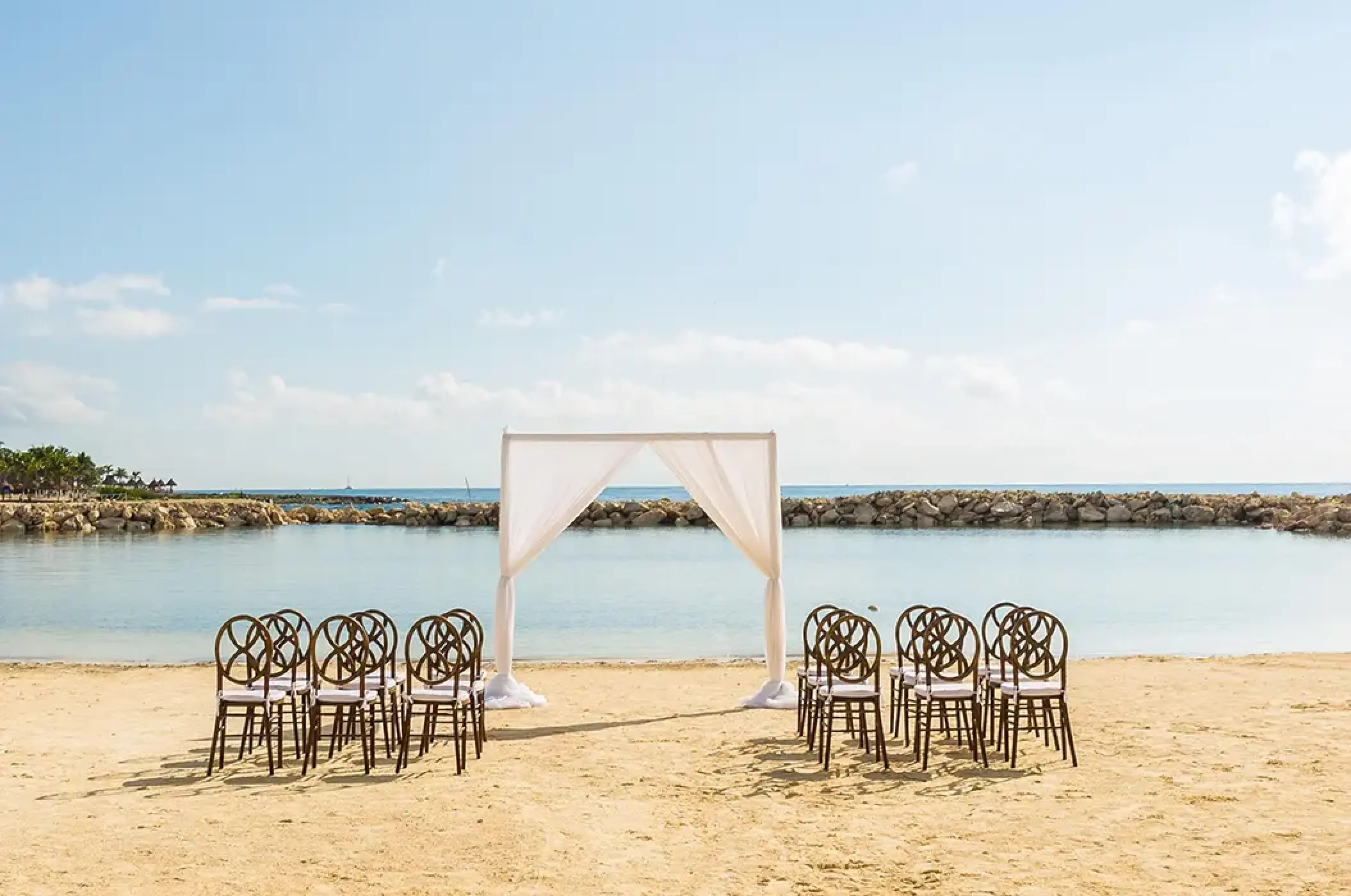 Beachfront wedding ceremony with white arch and wooden chairs at Dreams Aventuras, Riviera Maya