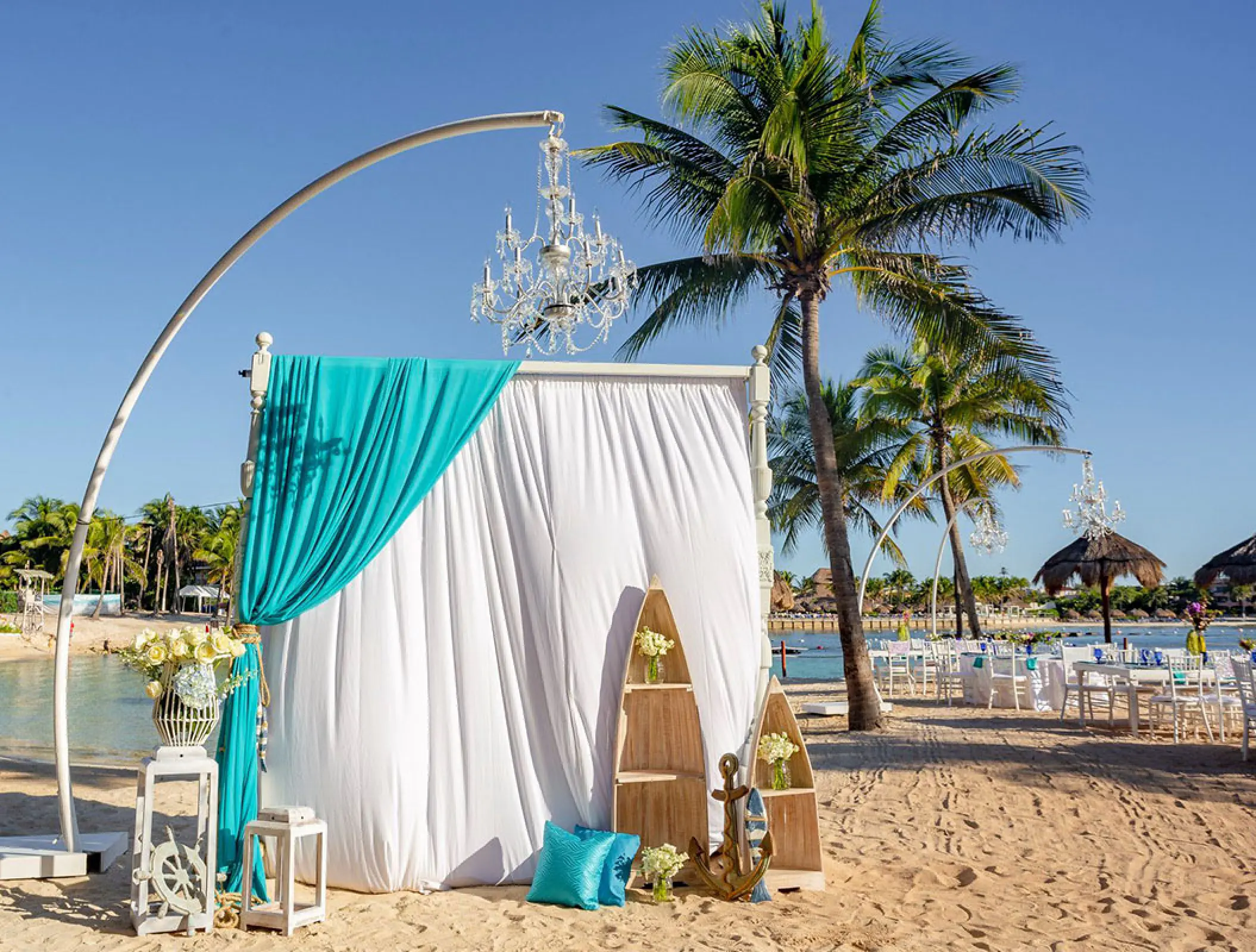 Beachfront wedding ceremony setup with white and turquoise draping and chandeliers at Dreams Aventuras, Riviera Maya