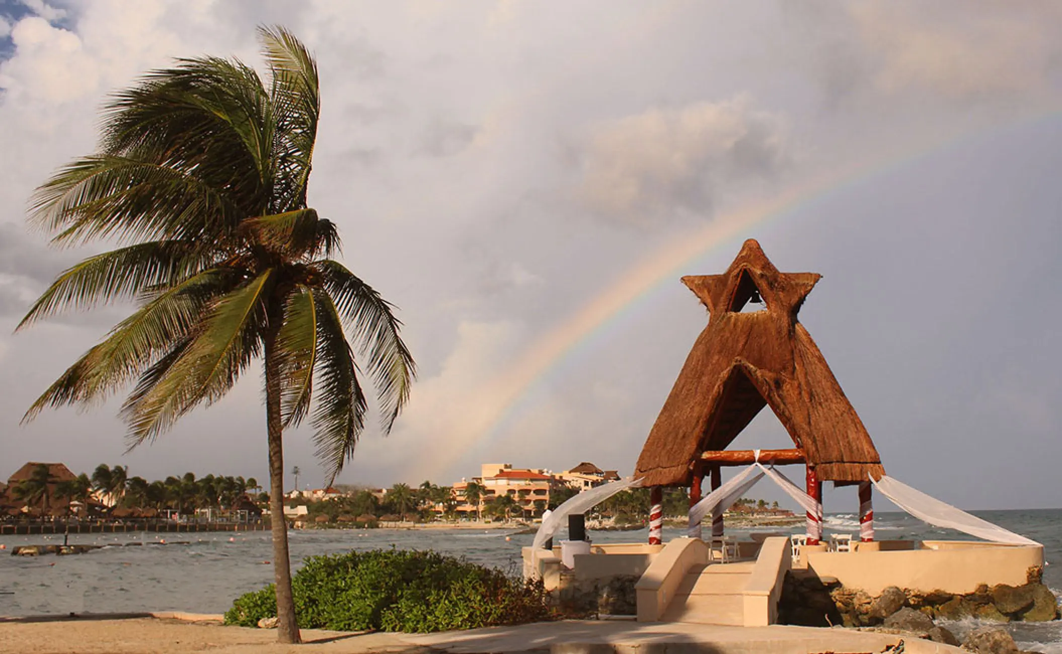 Thatched oceanfront wedding gazebo under a rainbow at Dreams Aventuras, Riviera Maya