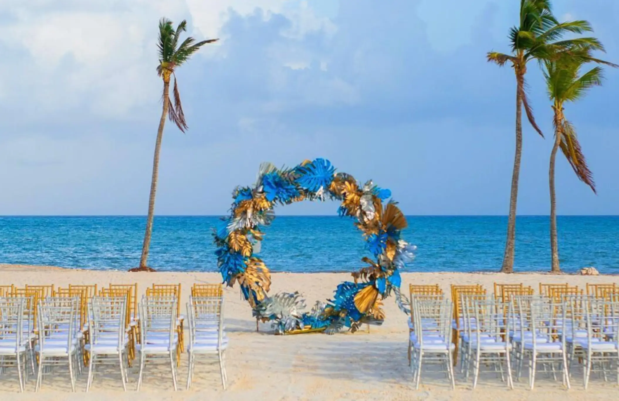 Beachfront wedding ceremony with circular floral arch and silver chairs at Dreams Cap Cana, Punta Cana