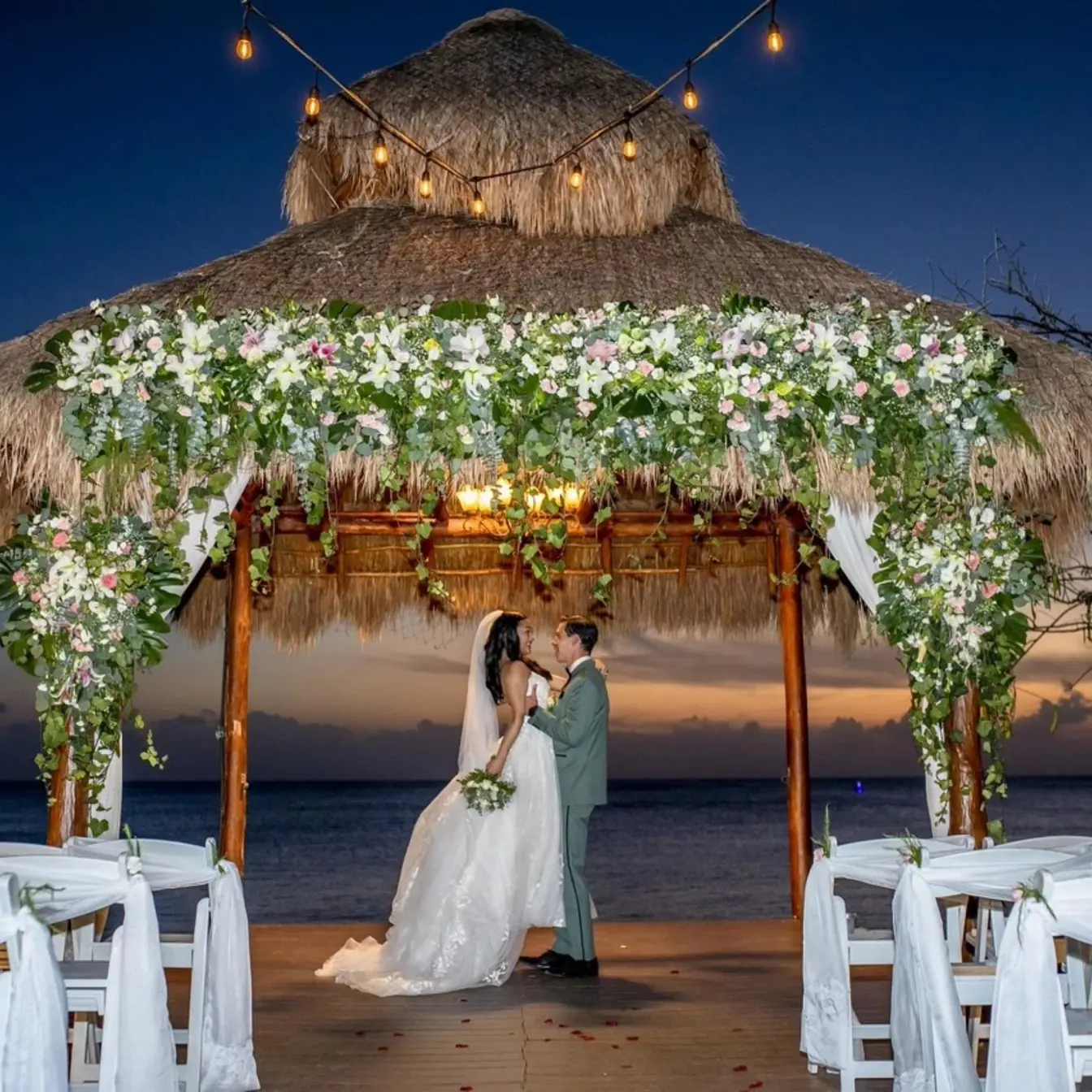 The bride and groom embracing under a thatched gazebo at Dreams Cozumel, Cozumel