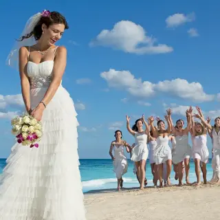 Bride holding a bouquet while bridesmaids run behind her on the beach at Dreams Cozumel, Cozumel