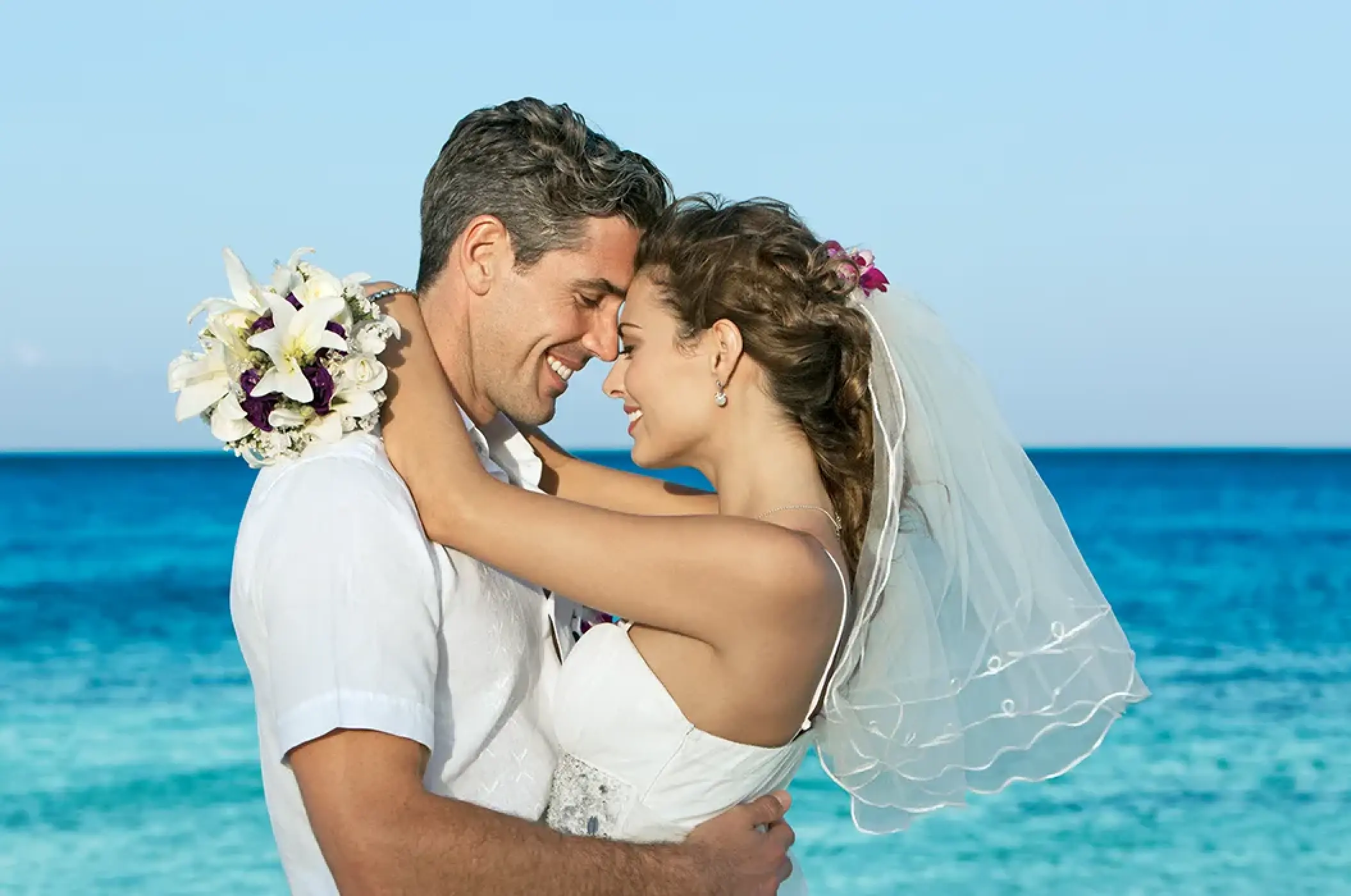 Bride and groom embracing by the turquoise ocean at Dreams Cozumel
