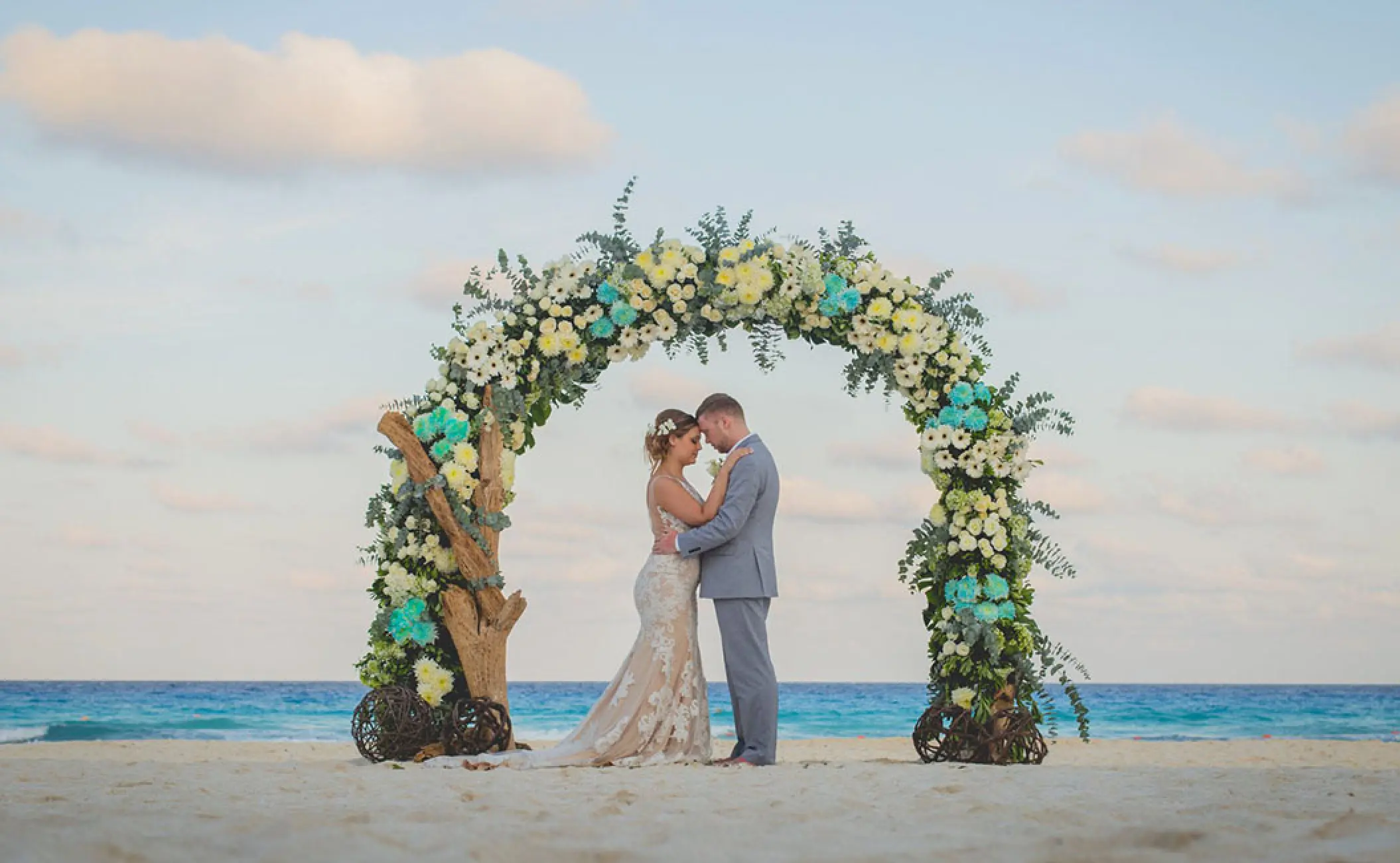 The bride and groom standing under a floral arch during a beach ceremony at Dreams Cozumel, Cozumel
