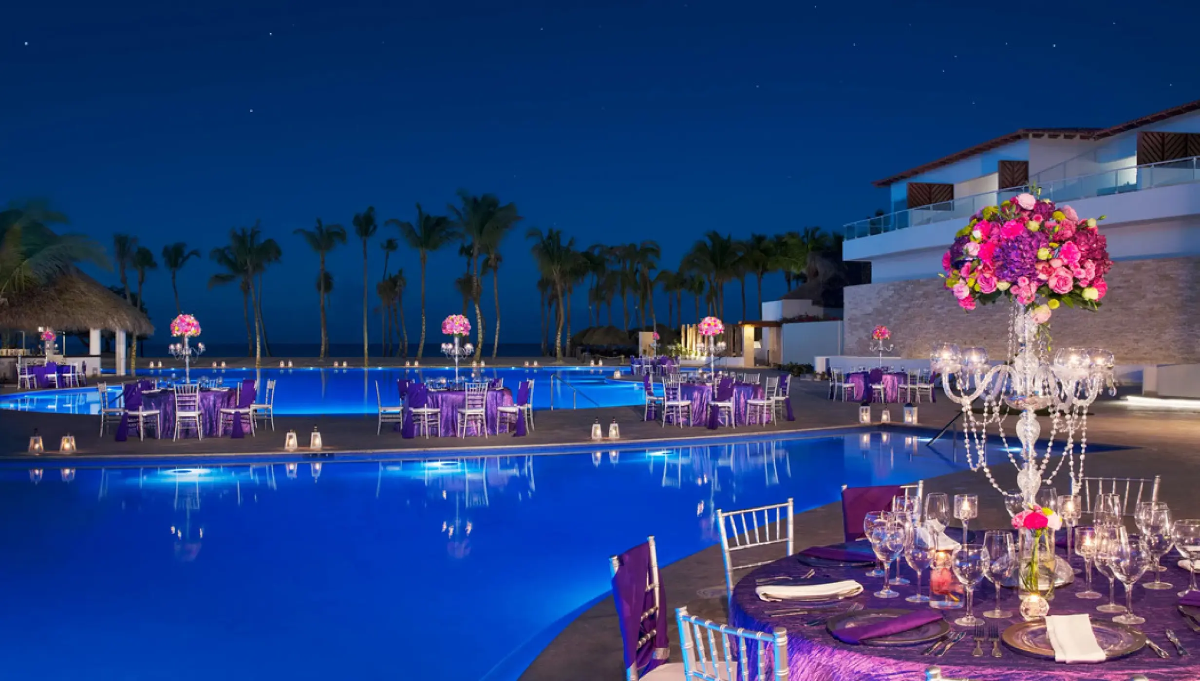 Poolside wedding reception at Dreams Dominicus, La Romana with purple decor and floral centerpieces at night