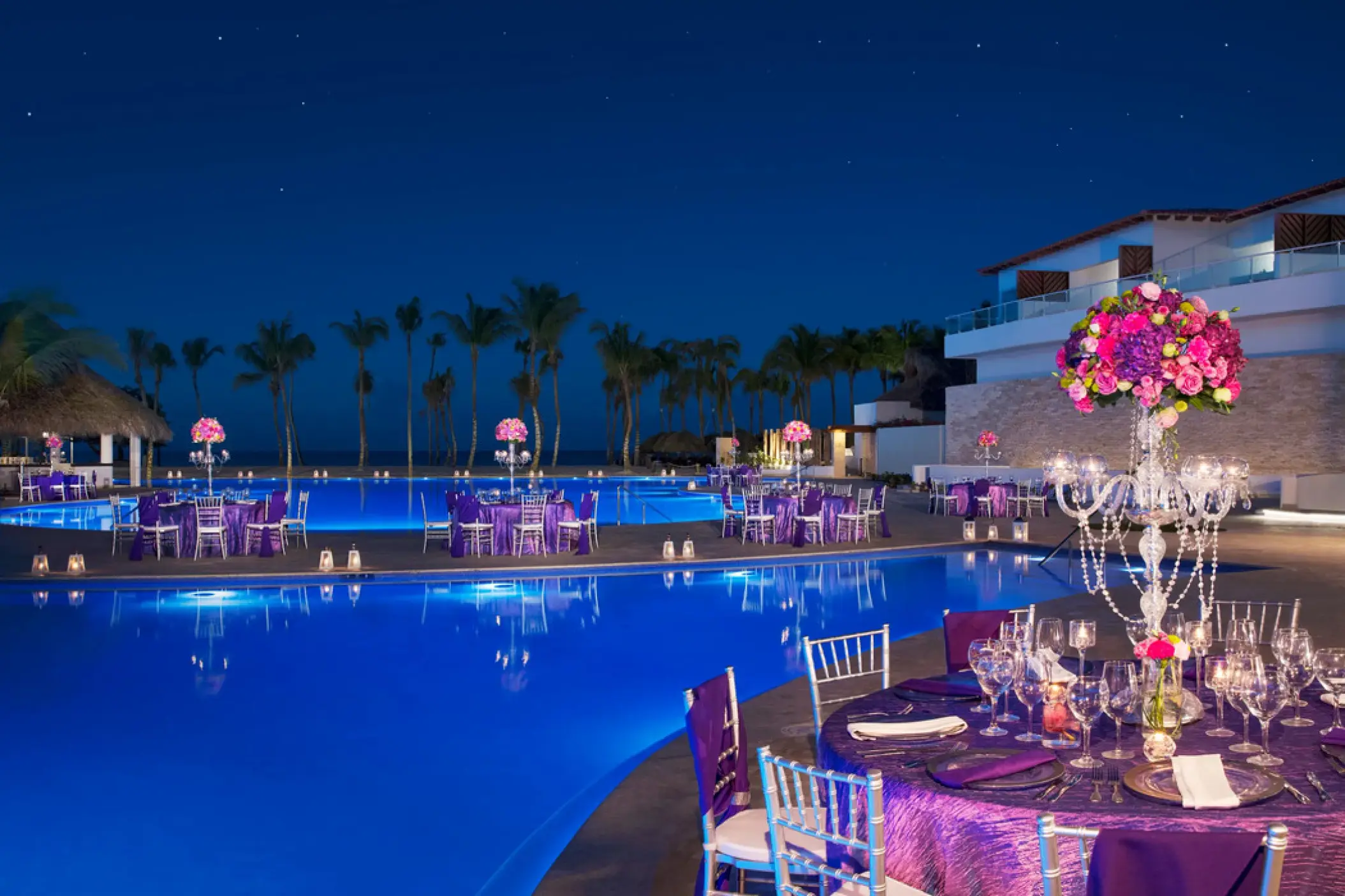 Poolside wedding reception at Dreams Dominicus, La Romana with purple decor and floral centerpieces at night