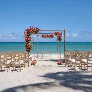 Beachfront wedding ceremony with a floral wooden arch and gold chairs at Dreams Flora, Punta Cana