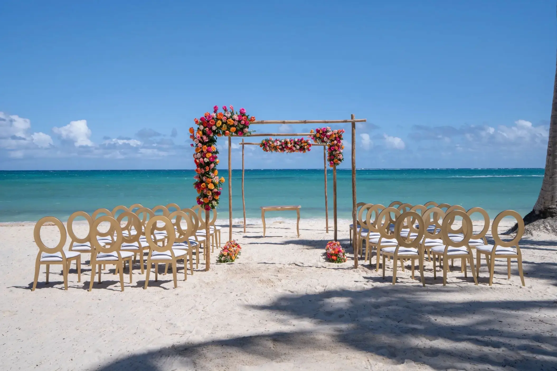 Beachfront wedding ceremony with a floral wooden arch and gold chairs at Dreams Flora, Punta Cana