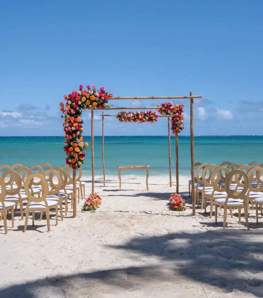 Beachfront wedding ceremony with a floral wooden arch and gold chairs at Dreams Flora, Punta Cana