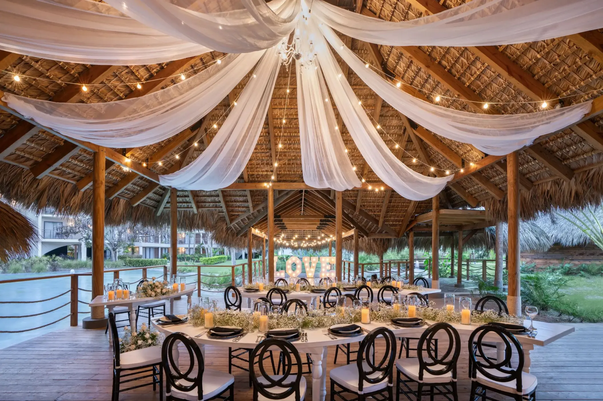 Wedding reception setup under a thatched palapa with white draping and string lights at Dreams Flora, Punta Cana
