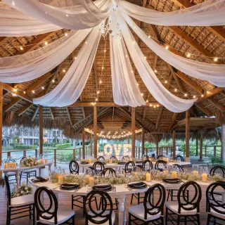 Wedding reception setup under a thatched palapa with white draping and string lights at Dreams Flora, Punta Cana