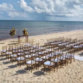 Beachfront wedding ceremony with wooden chairs and a floral arch at Dreams Jade, Riviera Maya