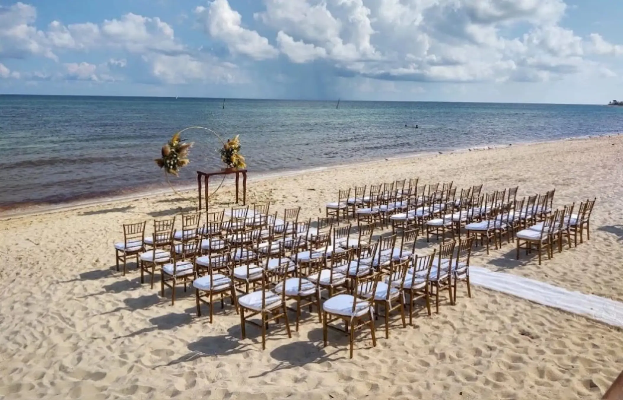 Beachfront wedding ceremony with wooden chairs and a floral arch at Dreams Jade, Riviera Maya