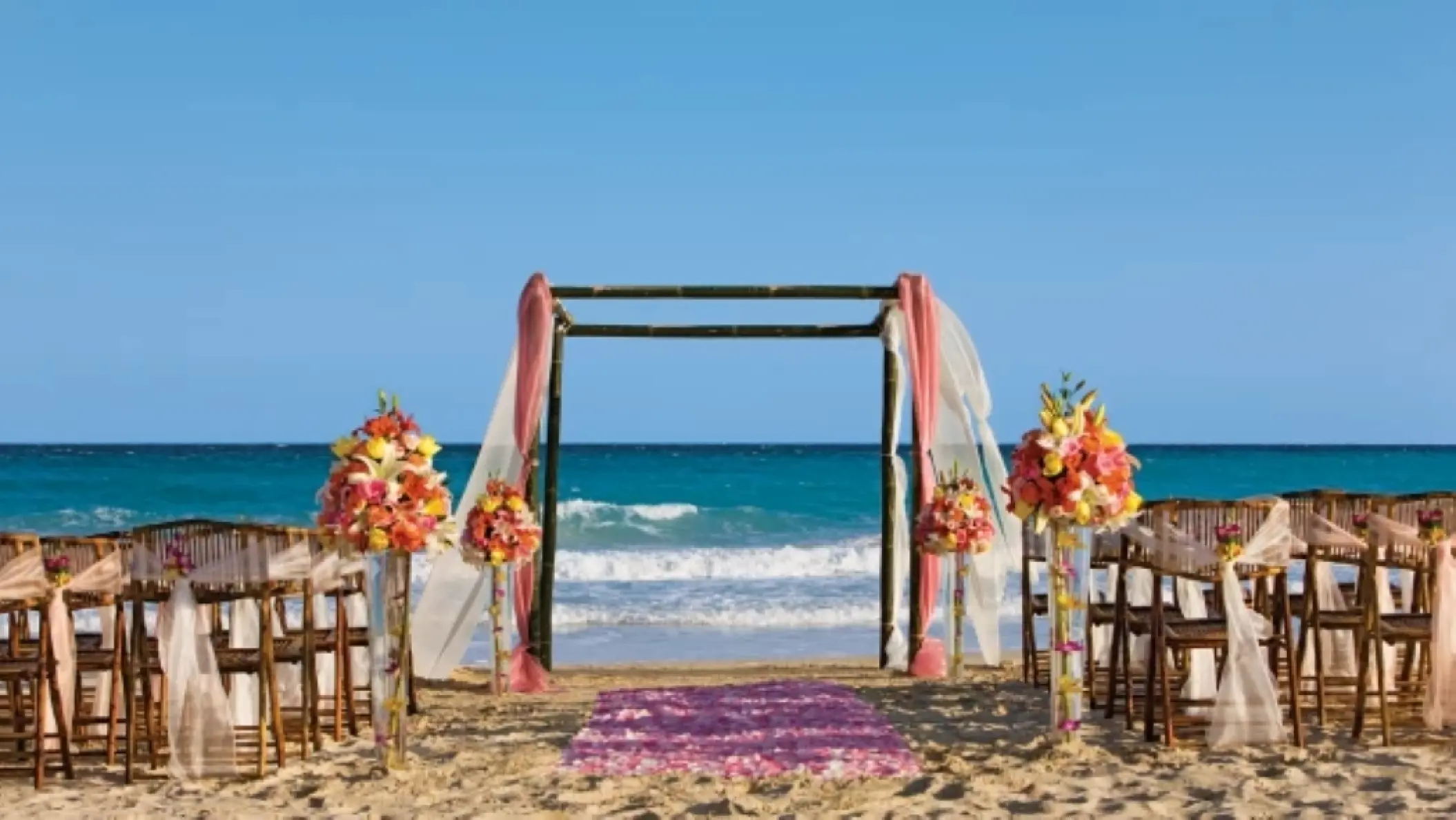 Beachfront wedding ceremony with a dark wood huppah and pink florals at Dreams Jade, Riviera Maya