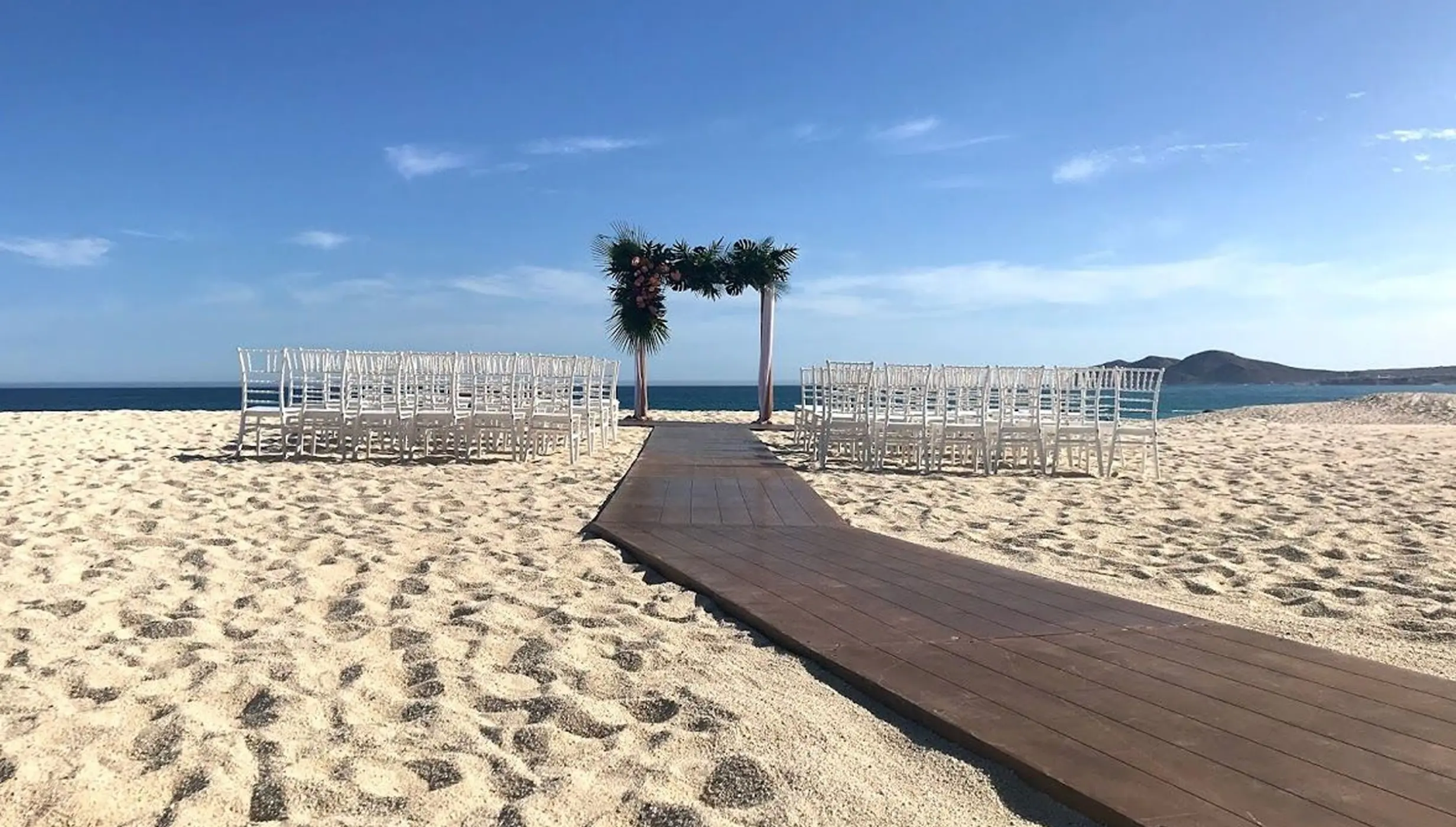 Beachfront wedding ceremony setup with white chairs and floral arch at Dreams Los Cabos, Cabo San Lucas