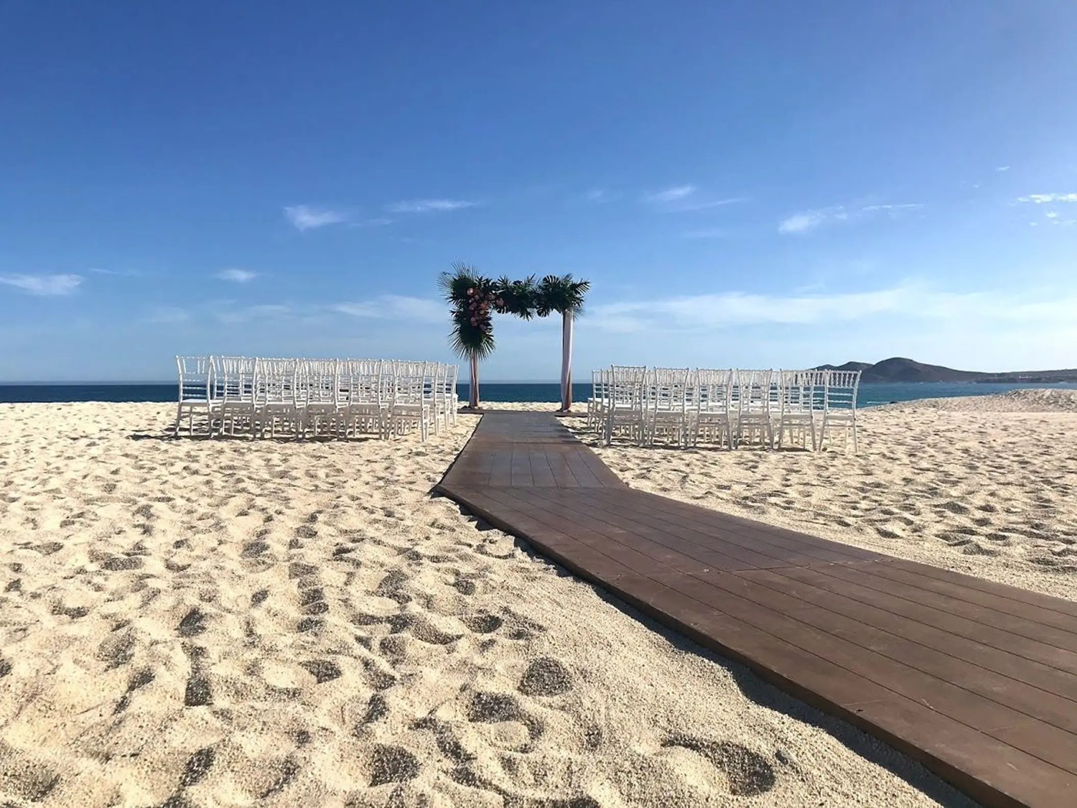 Beachfront wedding ceremony setup with white chairs and floral arch at Dreams Los Cabos, Cabo San Lucas