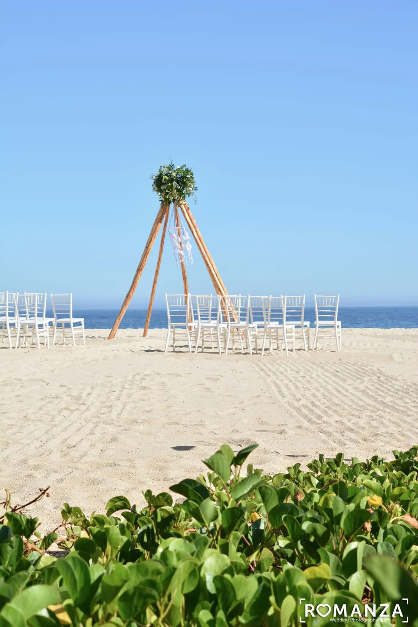 Beach wedding ceremony with a teepee-style arch and white chairs at Dreams Los Cabos, Cabo San Lucas