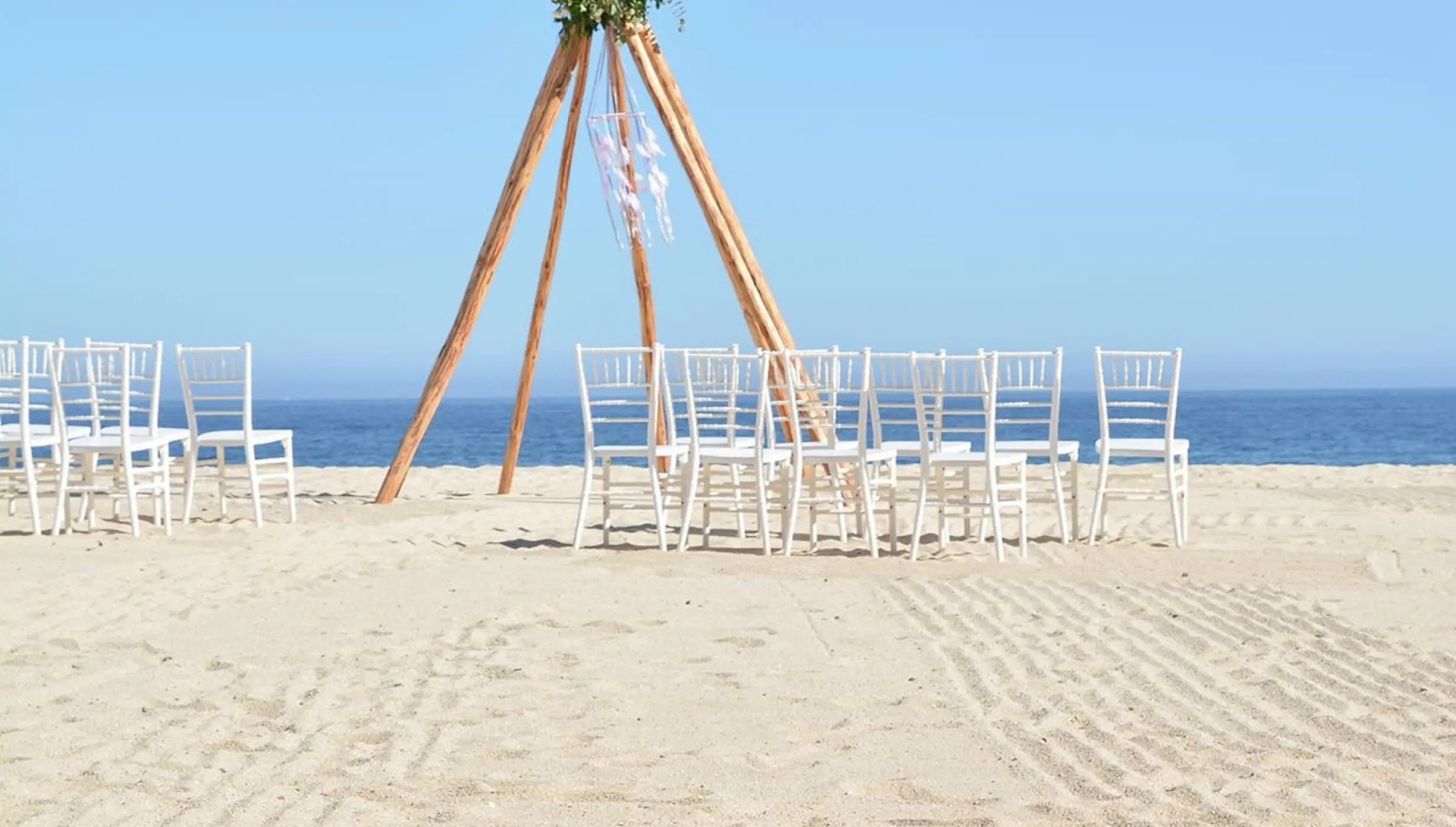 Beach wedding ceremony with a teepee-style arch and white chairs at Dreams Los Cabos, Cabo San Lucas