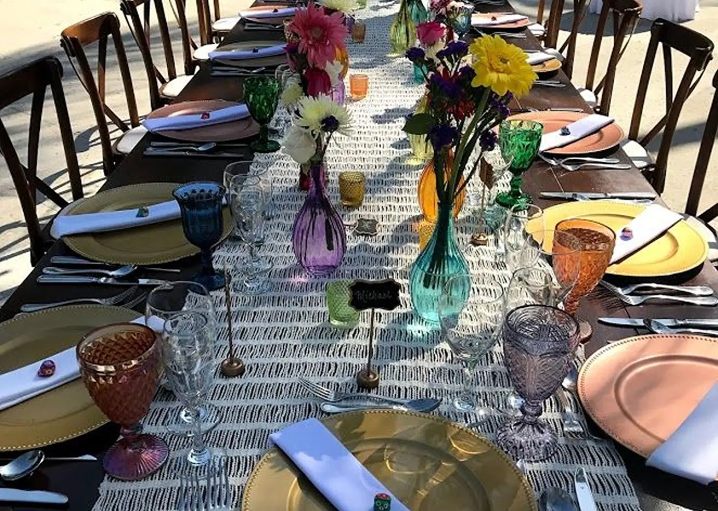 Long wooden wedding reception table with colorful glassware and floral centerpieces at Dreams Los Cabos, Cabo San Lucas