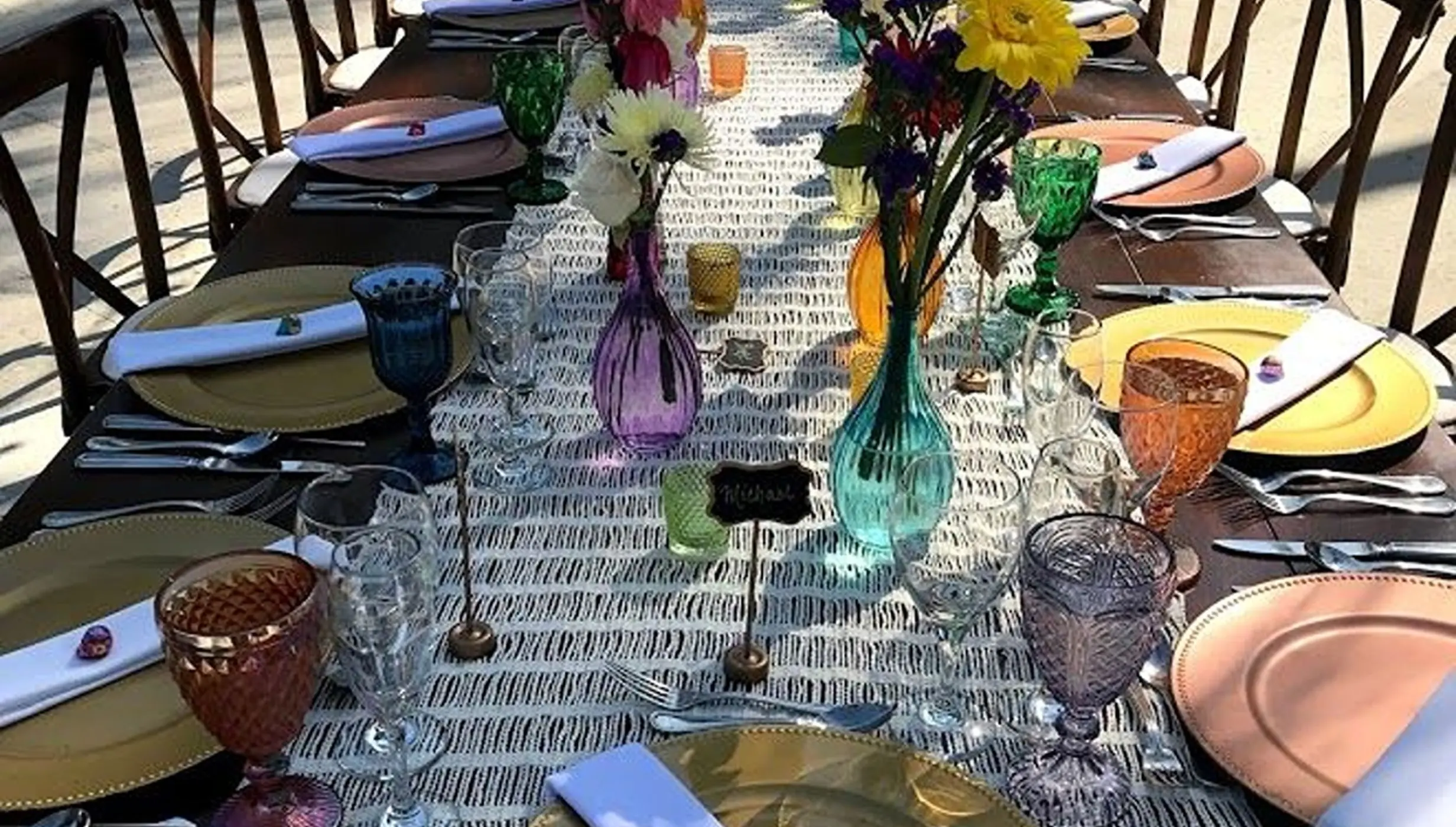 Long wooden wedding reception table with colorful glassware and floral centerpieces at Dreams Los Cabos, Cabo San Lucas