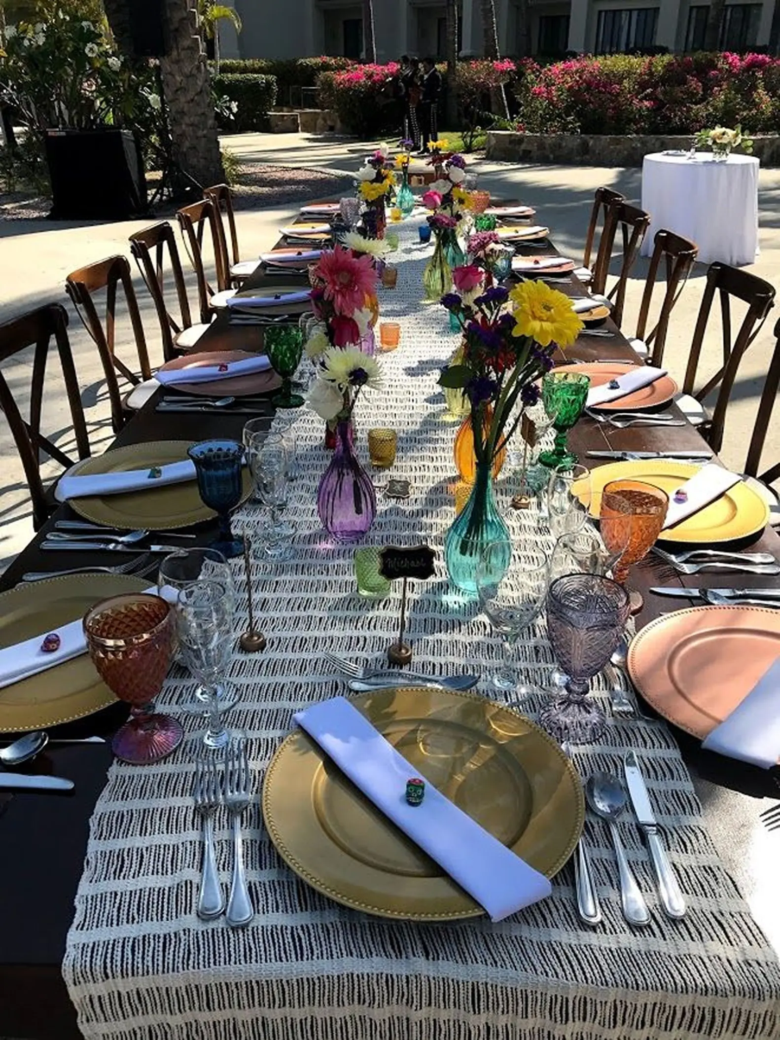 Long wooden wedding reception table with colorful glassware and floral centerpieces at Dreams Los Cabos, Cabo San Lucas