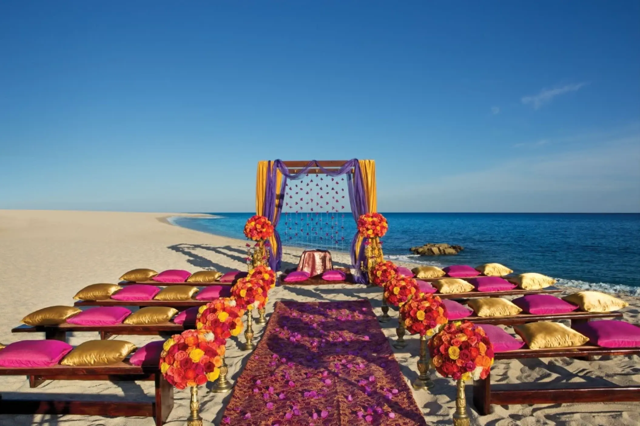Beach wedding ceremony setup with pink and gold seating at Dreams Los Cabos, Cabo San Lucas