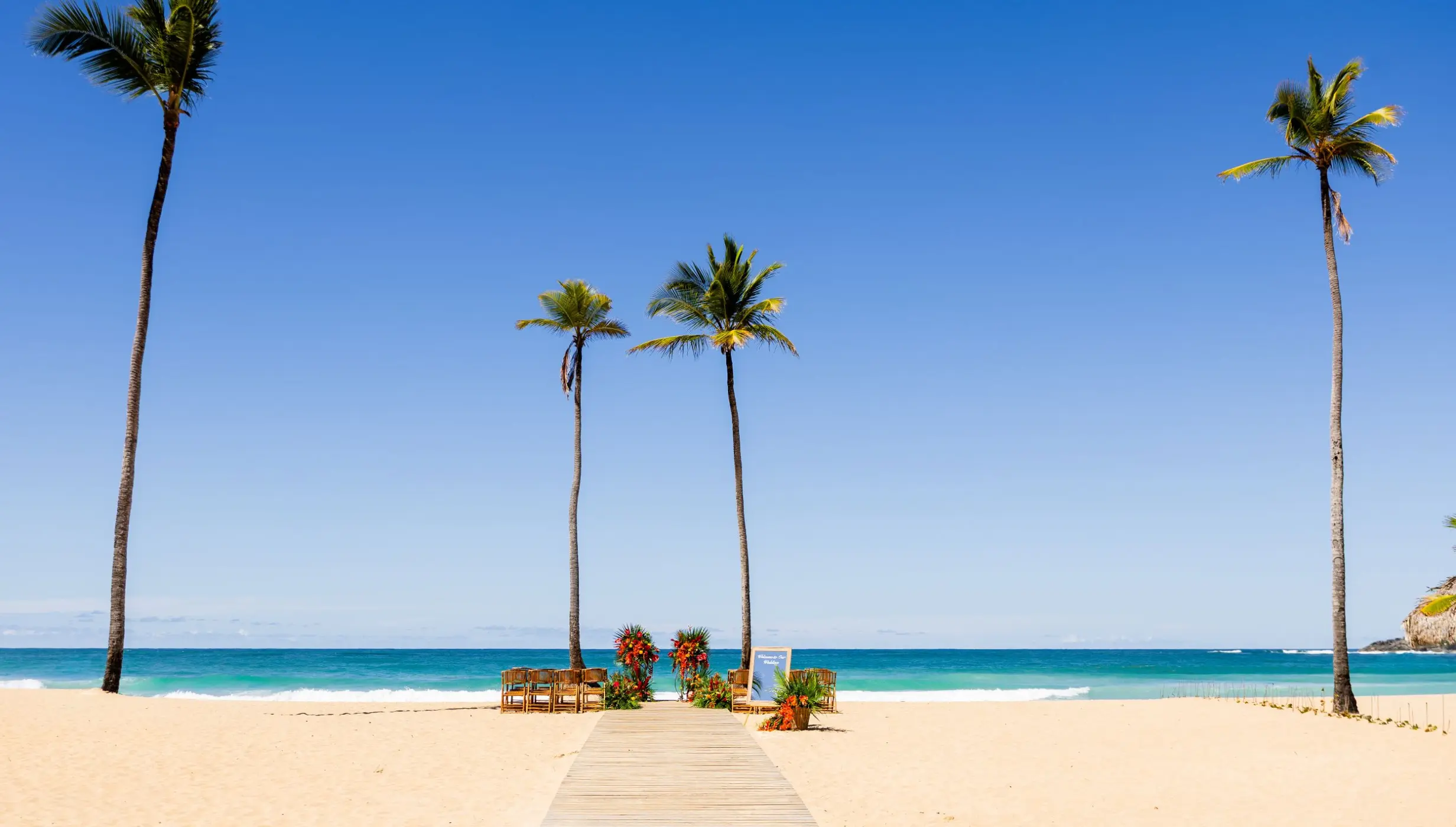 Wooden walkway leading to a beach ceremony setup with palm trees at Dreams Macao Beach, Punta Cana
