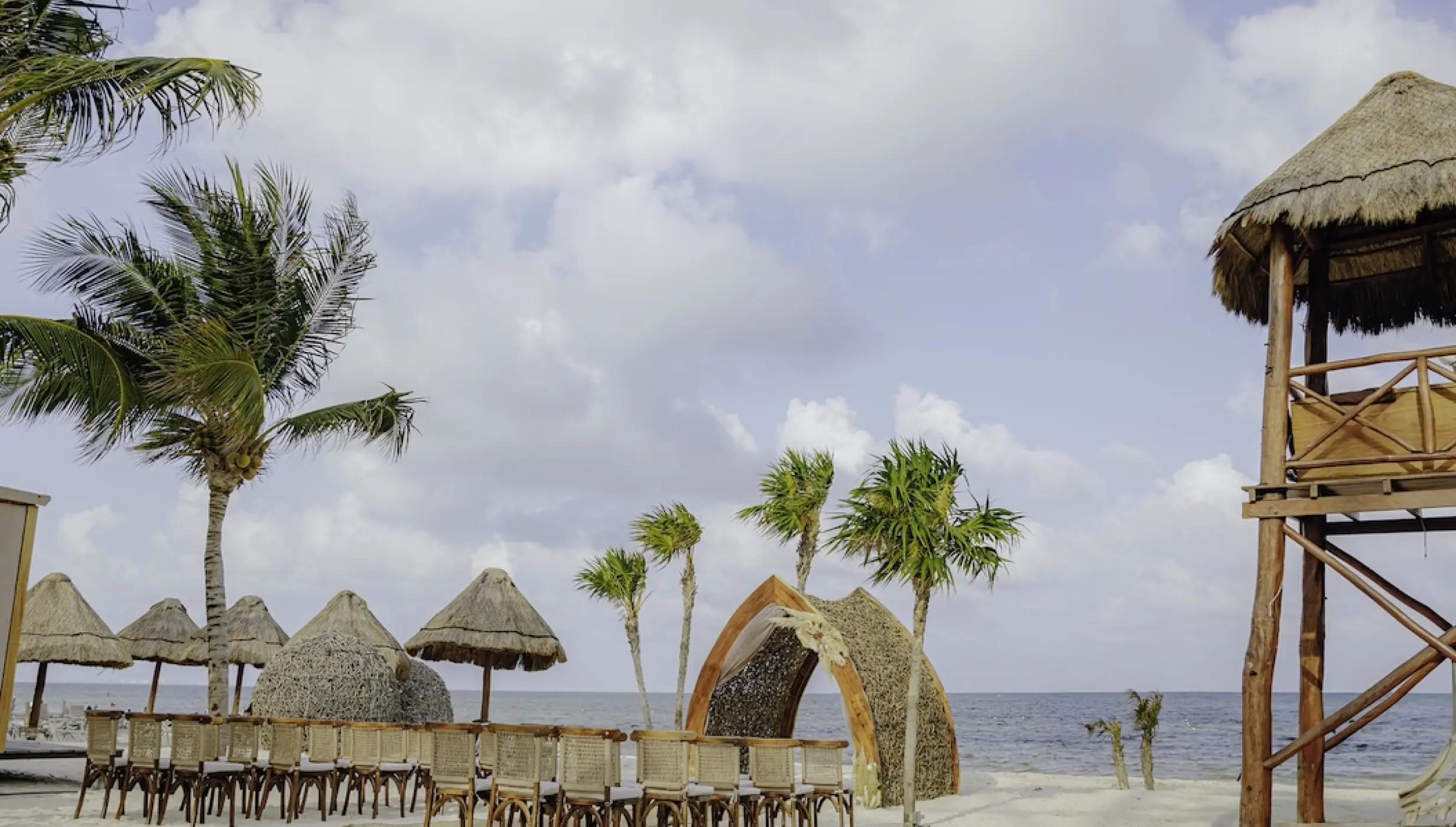 Beachfront wedding ceremony with thatched gazebo and wooden chairs at Dreams Natura, Riviera Maya