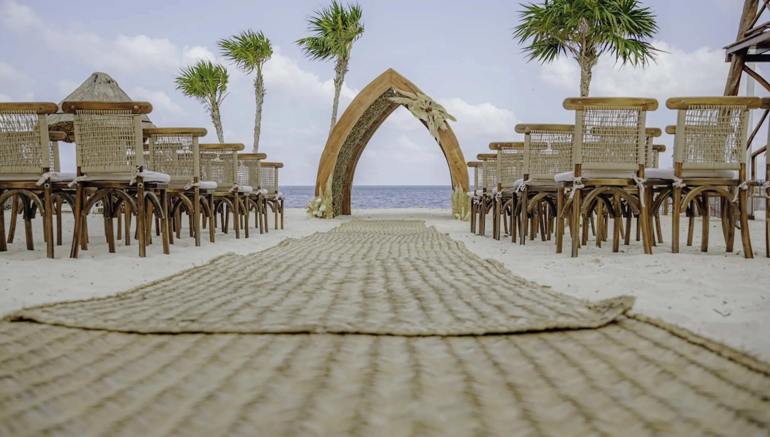 Beachfront wedding ceremony with a woven aisle and pointed wooden arch at Dreams Natura, Riviera Maya