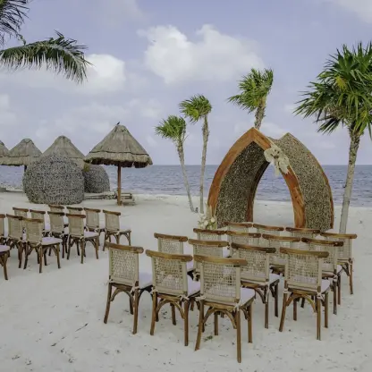 Beachfront wedding ceremony with wooden chairs and a thatched gazebo at Dreams Natura, Riviera Maya