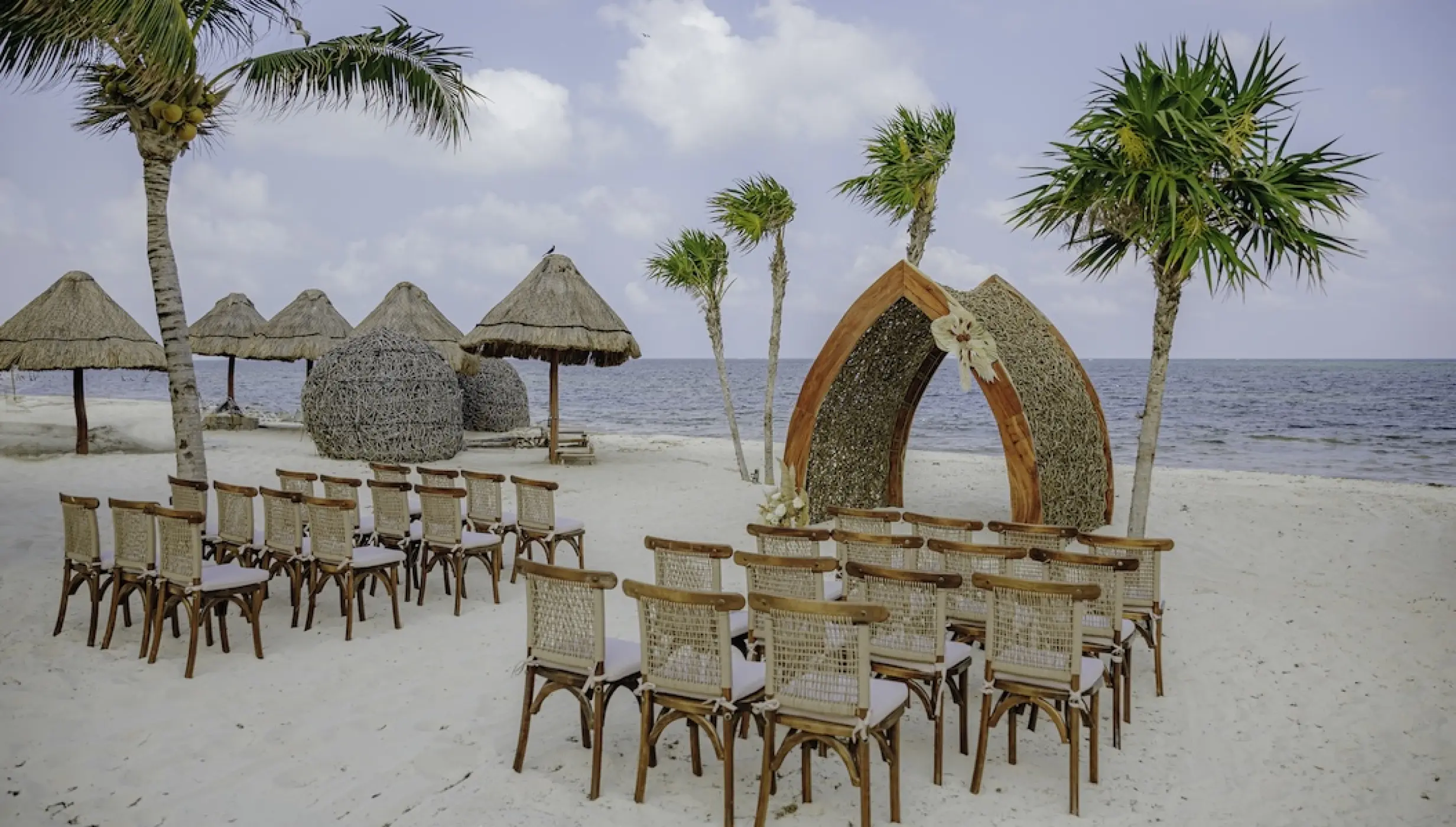Beachfront wedding ceremony with wooden chairs and a thatched gazebo at Dreams Natura, Riviera Maya