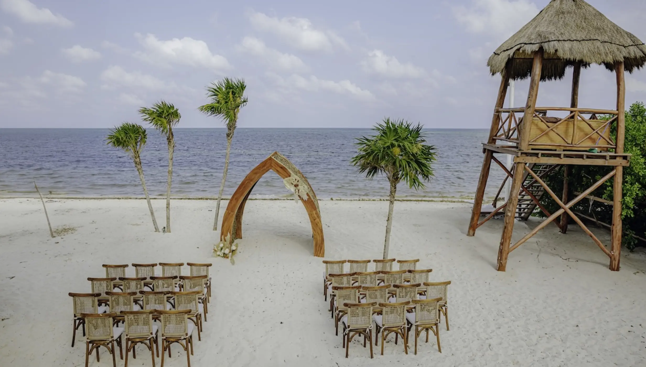 Beachfront wedding ceremony with a wooden arch and seating at Dreams Natura, Riviera Maya