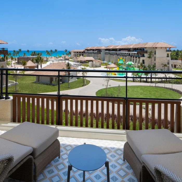 A balcony with lounge chairs offering a partial ocean view of the resort and its pools and water park.